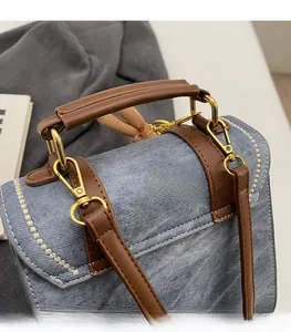 Detail of vintage denim crossbody bag with brown leather handle and golden hardware