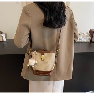 Détail du sac seau en toile avec bordure en cuir et pendentif de poupée dans un café