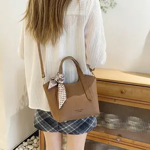 Sac seau en cuir marron avec foulard décoratif et bandoulière porté par un mannequin