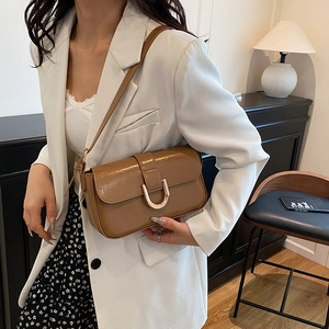 Brown vintage baguette shoulder bag with gold horseshoe buckle on a model in white blazer