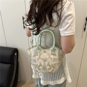 Floral embroidery bucket bag with green leather straps and handles in home setting