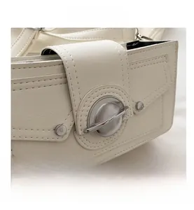 Close-up of white cross-grain leather shoulder bag with large round metal buckle and rivets