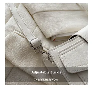 Detail view of the silver adjustable buckle and fine texture on a beige crossbody bag