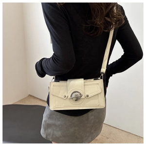Detail of off-white leather crossbody bag featuring a silver circular buckle and slim strap