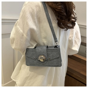 Détail d'un sac bandoulière gris avec boucle planète en métal et rivets élégants