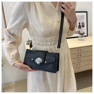 Detail of a black rectangular crossbody bag with silver planet buckle on a cream dress