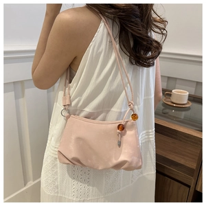 Detalle de bolso nube plisado rosa con cuentas de ámbar sobre un vestido blanco