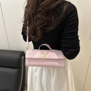 Pink woven texture crossbody bag with gold buckle and top handle shown on model