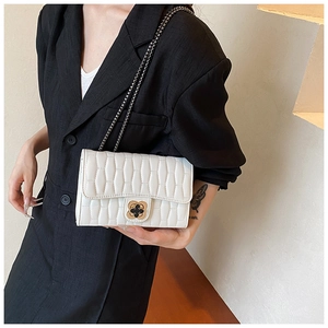 Detailed shot of white quilted crossbody bag with gold clover lock on black blazer