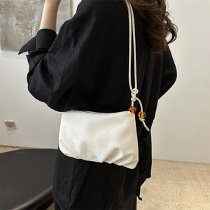 Sac à bandoulière froncé blanc en satin avec perles ambrées porté par un mannequin