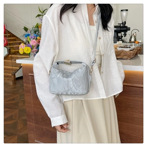 Silver wrinkled PU leather crossbody bag with gold lock shown in a cafe setting
