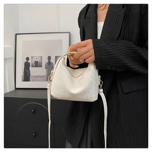 Detail of white textured crescent handbag with golden zipper and slender shoulder strap