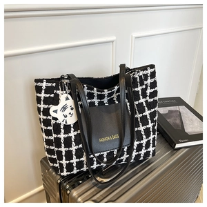 Detail of checkered tote bag with leather pocket and cute white tiger charm on a suitcase