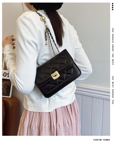 Detail of black quilted chain bag with gold hardware worn by a model in casual style
