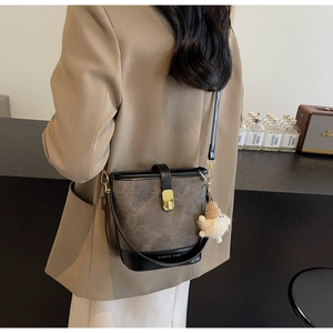 Détail du sac seau gris avec boucle dorée et pendentif en peluche porté à l'épaule
