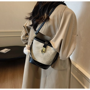 Détail d'un sac seau beige et noir avec boucle dorée et breloque peluche sur un manteau