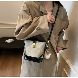 Détail du sac seau rétro avec tissu crème, finitions noires et charm pompon rouge élégant
