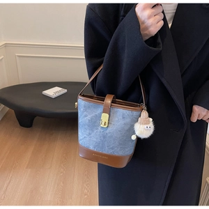 Détail du sac seau en daim bleu avec base en cuir marron et fermoir rotatif doré
