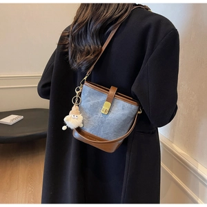 Détail du sac seau en denim bleu avec bordure en cuir marron et pendentif en peluche