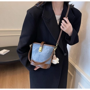 Détail d'un sac seau en denim bleu avec garniture en cuir marron et pompon blanc doux