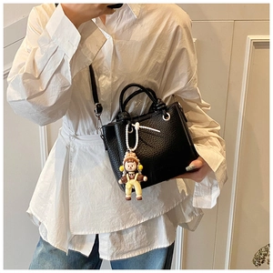 Detail of black lychee textured leather bucket bag with a cute 3D doll charm and strap