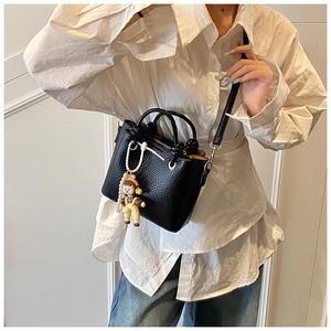 Close-up of black lychee leather crossbody bucket bag with a cute doll pendant charm