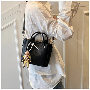 Side view of model wearing black litchi grain leather bucket bag with cute doll charm