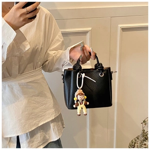 Detail of black pebbled leather bucket bag with knot handle and cute cartoon charm