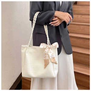 Chic cream tote bag with woven handles and silk scarf detail shown on model in a staircase