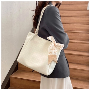 Chic white tote bag featuring a woven handle and silk scarf detail on wooden stairs