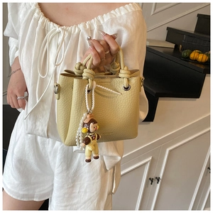 Detail of yellow bucket bag with litchi texture, knotted handle and pearl charm