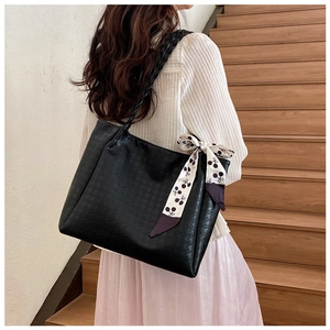 Close-up of black tote bag with houndstooth embossing, cherry scarf, and woven strap