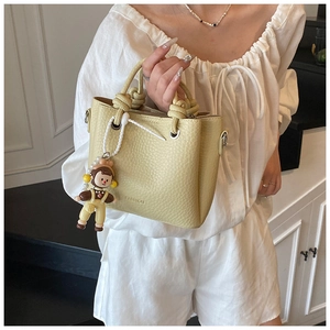 Detail of light yellow bucket bag with litchi texture and cute doll charm accessory