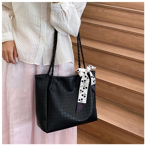 Detail of black textured tote bag with decorative polka dot ribbon on a woven handle