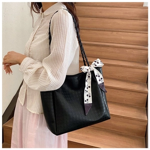 Close-up of a large black textured tote bag with a cherry pattern scarf on a wooden staircase