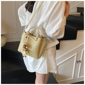 Detail of creamy yellow bucket bag with lychee texture and cute bear charm pendant