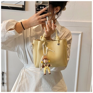 Close-up of yellow textured bucket bag with fashion lettering and cute cartoon doll charm