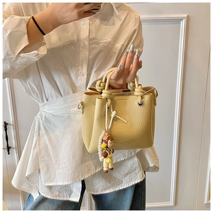 Detail of lychee textured bucket bag featuring knot handle and pearl doll pendant