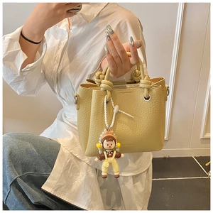 Detail of yellow lychee leather bucket bag with knotted handles and a cute doll charm