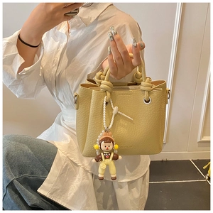 Close-up of beige leather bucket bag with knot handle and cartoon girl charm pendant