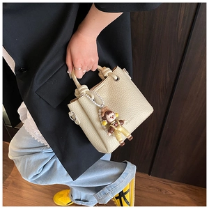 Detail of cream bucket bag with litchi grain texture, fashion logo and cute charm