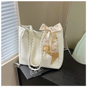 Detailed view of a white tote bag with woven handles and silk scarf on a black shelf
