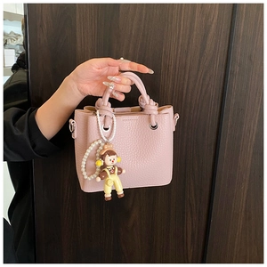 Detail of pink bucket bag with woven handle, pearl chain, and cute cartoon girl charm