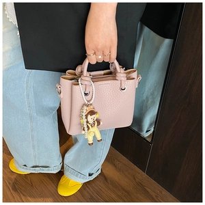 Detail of pink lychee leather bucket bag with cute doll charm and pearl chain decoration