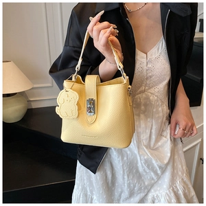 Détail d'un sac seau en cuir jaune pâle avec fermoir rotatif argenté et breloque en chien