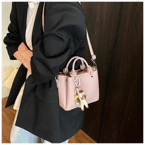 Side view of small pink bucket bag with pearl doll pendant on a model