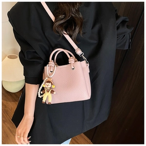 Pink lychee grain bucket bag with pearl charm shown worn as a crossbody bag