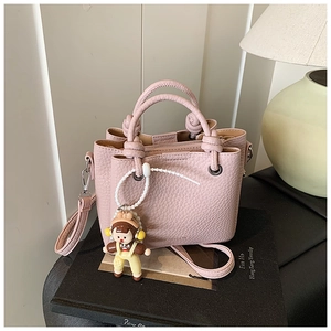 Detail of pink lychee leather bucket bag with woven handles and a cute girl charm