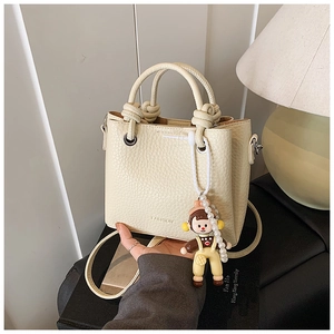Close-up of beige leather bucket bag with cute doll charm and pearl chain detail