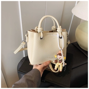 Detail of beige litchi grain bucket bag with FASHION logo and cute pearl charm